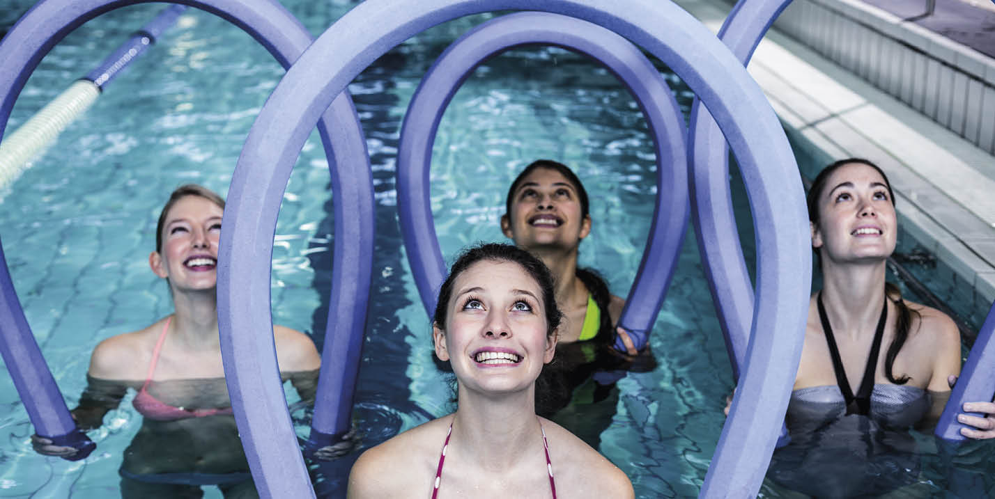 Happy fitness class doing aqua aerobics with foam rollers in the pool