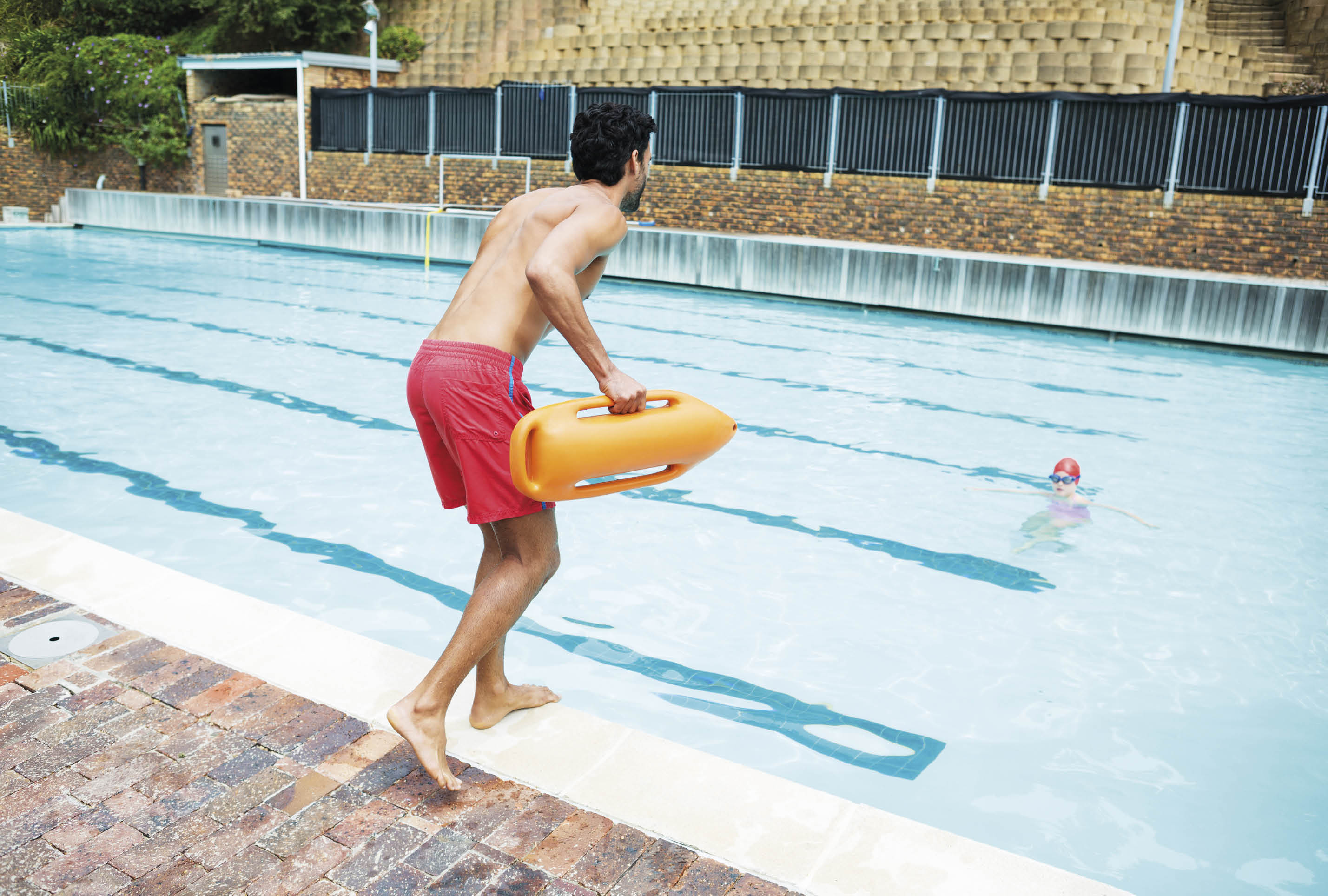 Rear view of lifeguard jumping into a swimming pool to rescue drowning boy