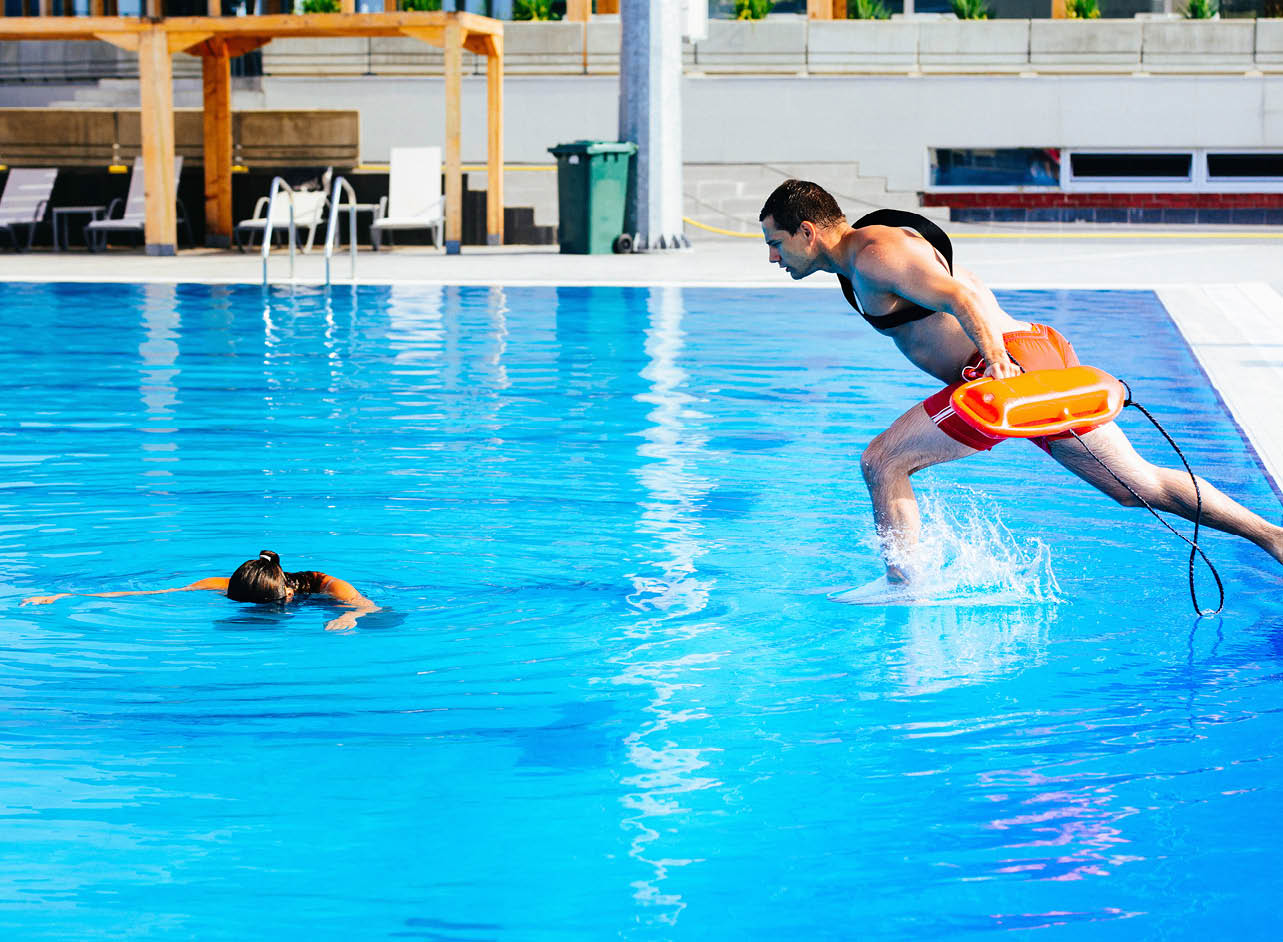 Lifeguard rescue training - young man jumping into a swimming pool to rescue drowning victim