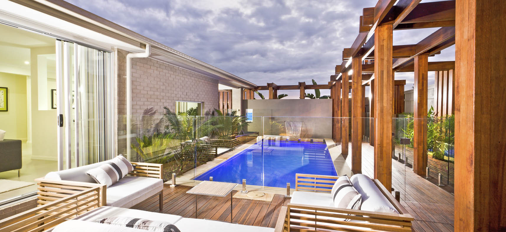 Wood decorated swimming pool area with green plants and glass panel cover under the cloudy sky in a modern house or hotel